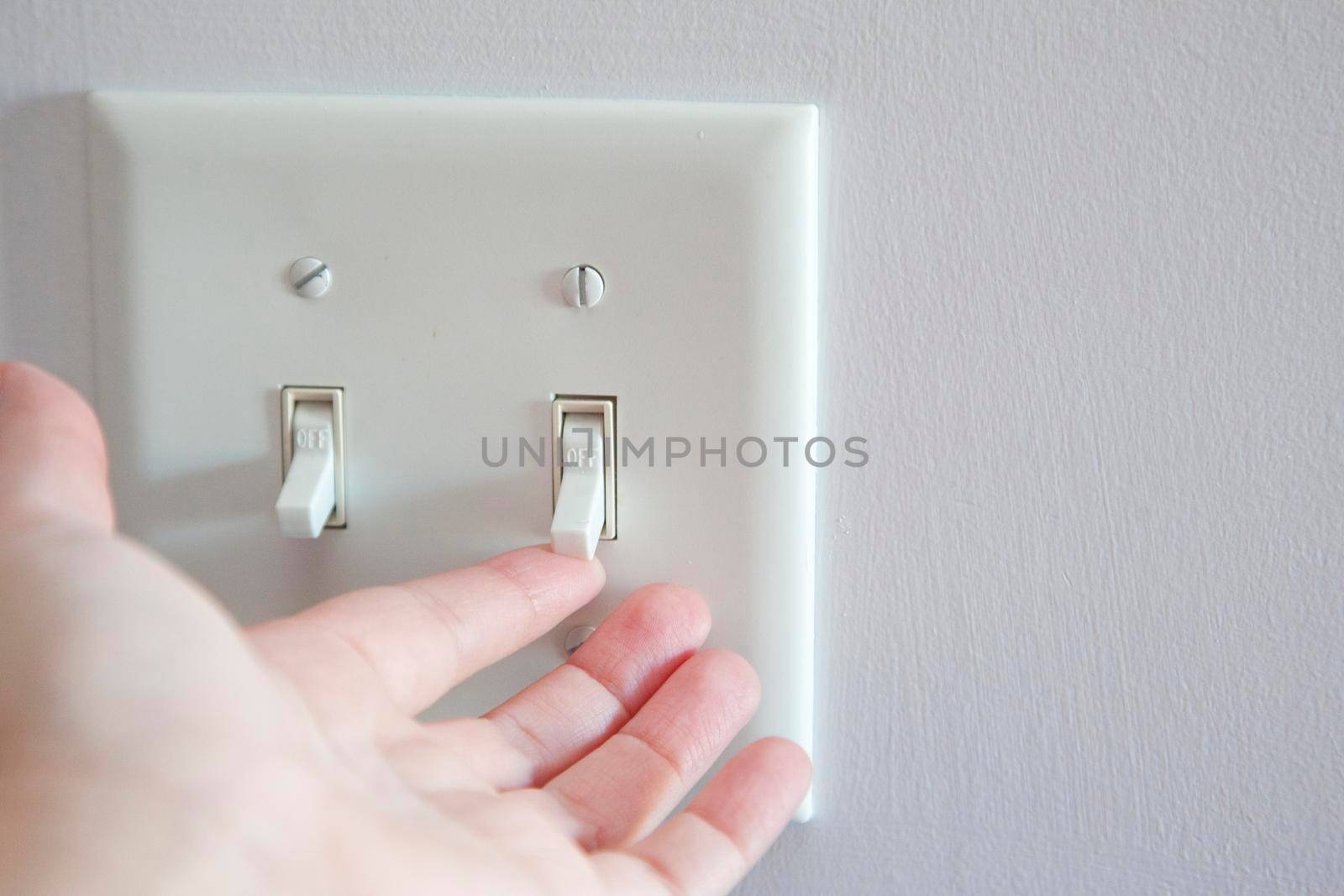 Hand about to turn a light switch from the off position to on 