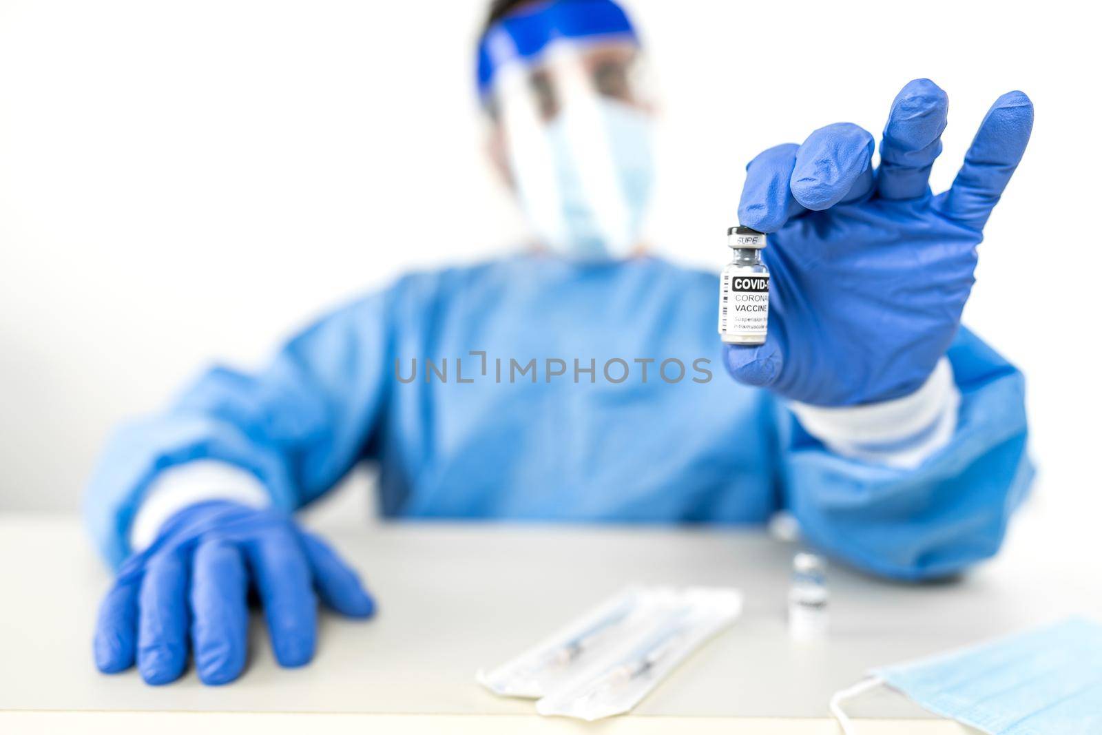 Concept of global vaccination to fight Covid-19 pandemic: medical or health worker in full protection safe kit with blue gloves showing to the camera a vial of Coronavirus vaccine in selective focus by robbyfontanesi