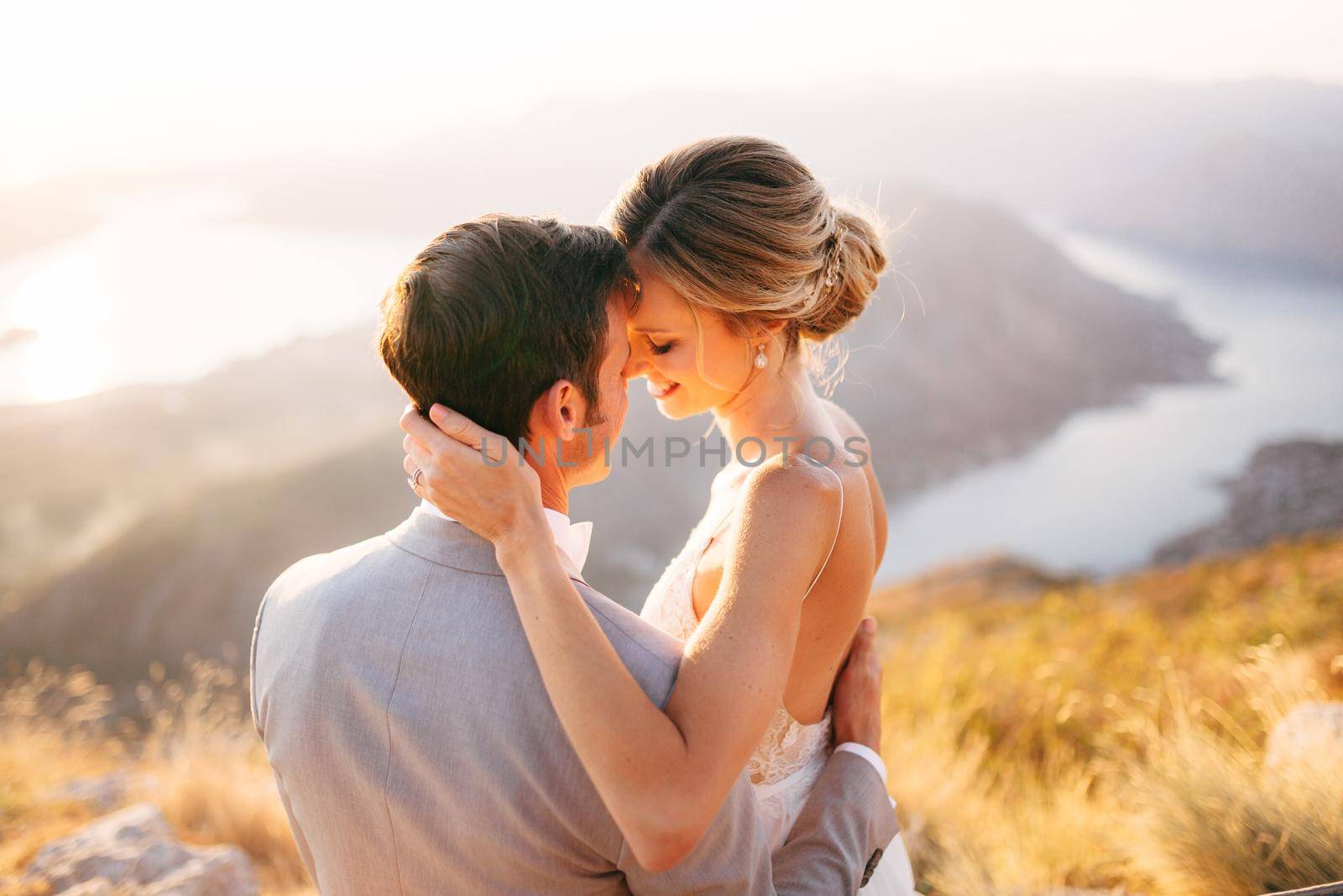 The bride and groom sitting on the top of Mount Lovcen overlooking the Bay of Kotor, smiling and hugging tenderly, close-up by Nadtochiy