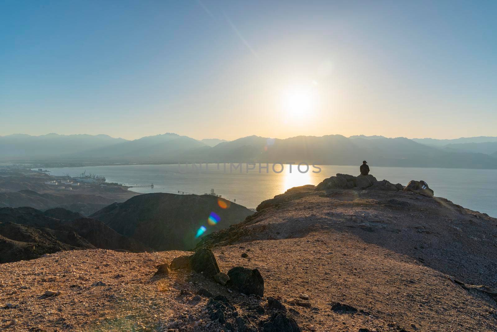 A man sits on a high mountain cliff and overlooks the sunrise and the horizon. A concept for hope, peace, power, soul searching. Desert mountains against the backdrop of the Red Sea. Shlomo mountain, Eilat Israel