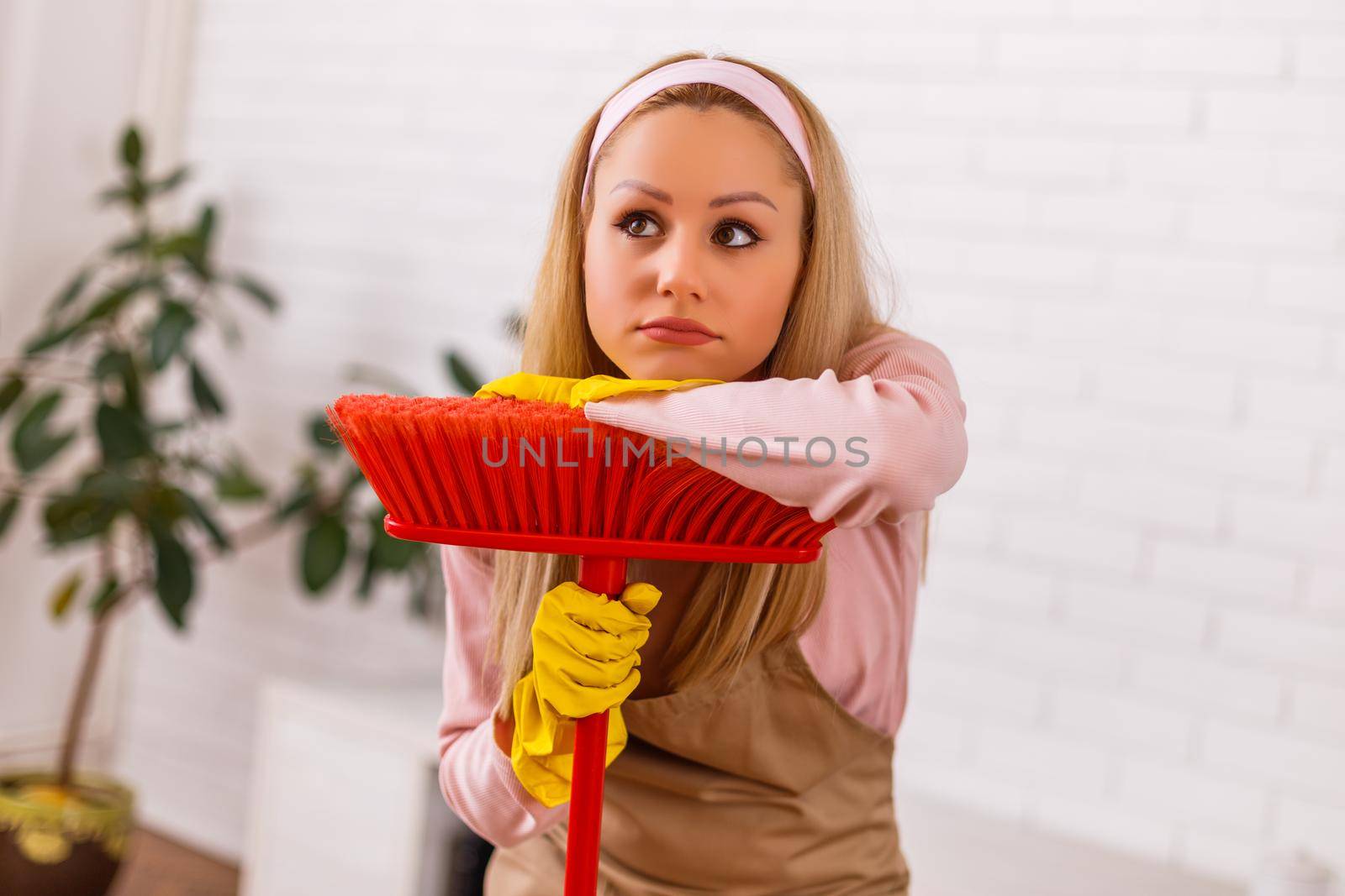 Tired housewife cleaning living room with a broom.