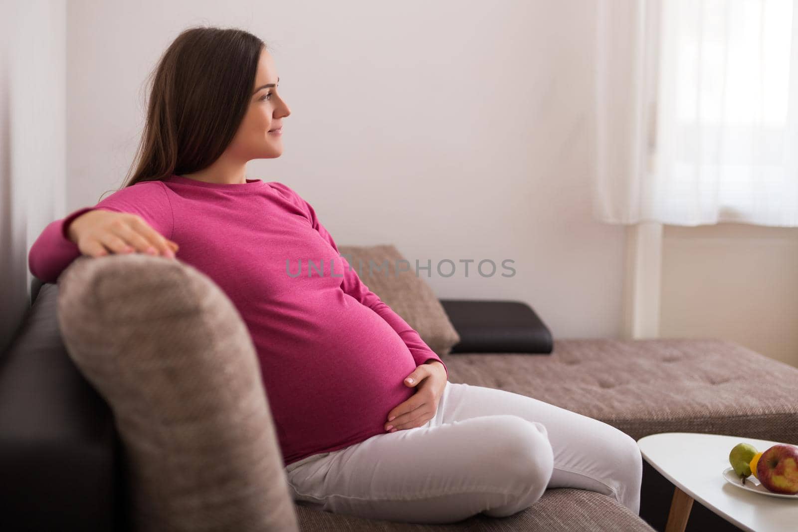 Beautiful pregnant woman enjoys resting on sofa at her home.