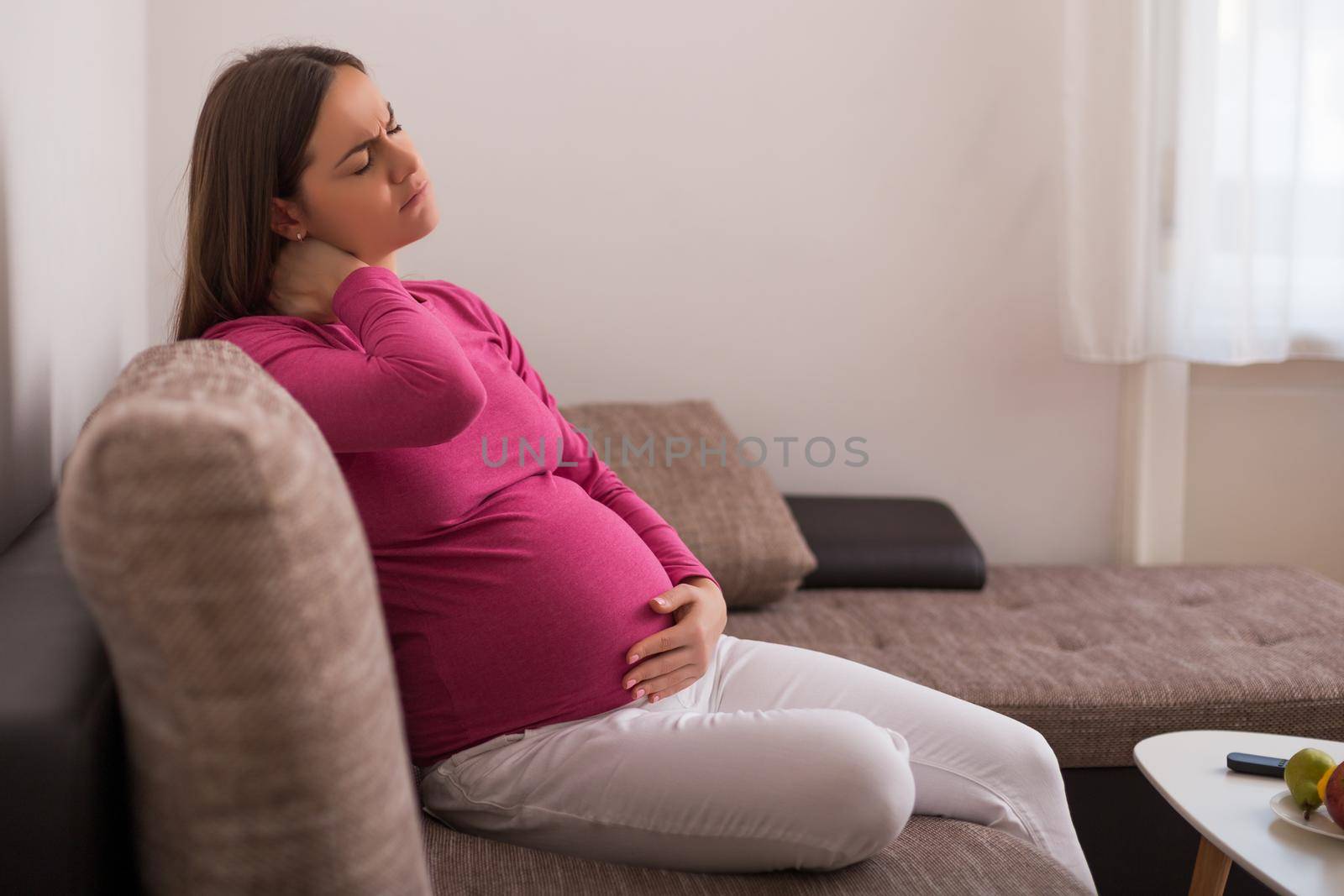 Pregnant woman having neck pain while spending time at her home.