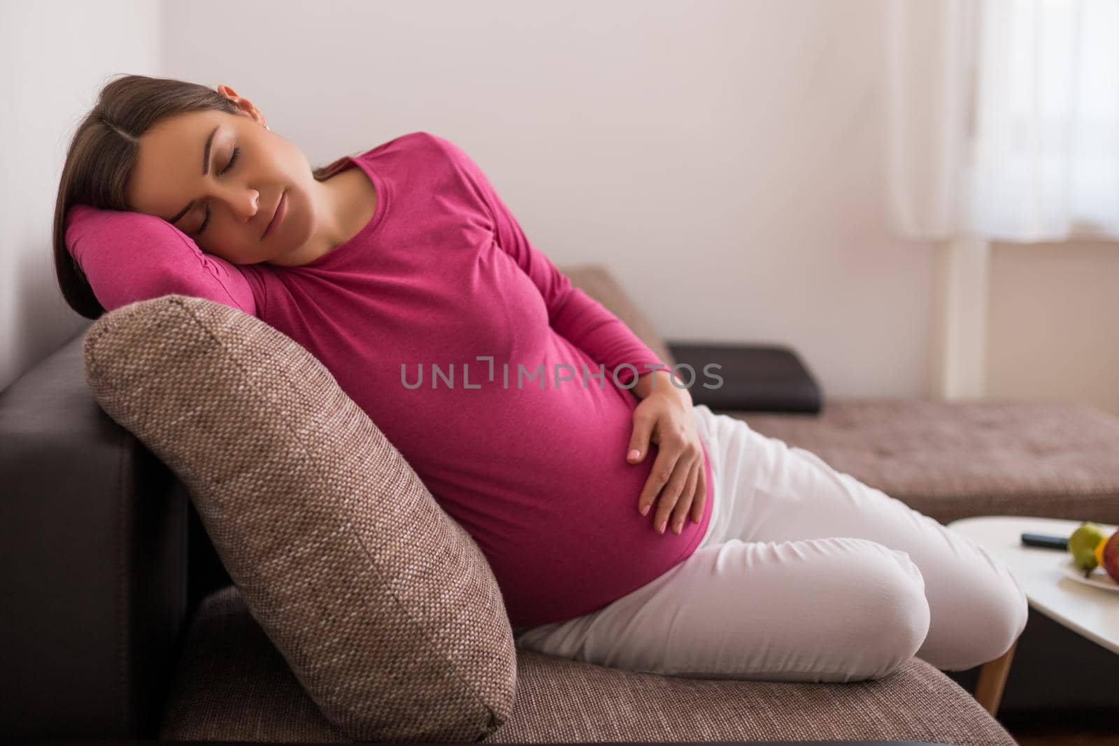 Beautiful pregnant woman enjoys sleeping on sofa at her home.