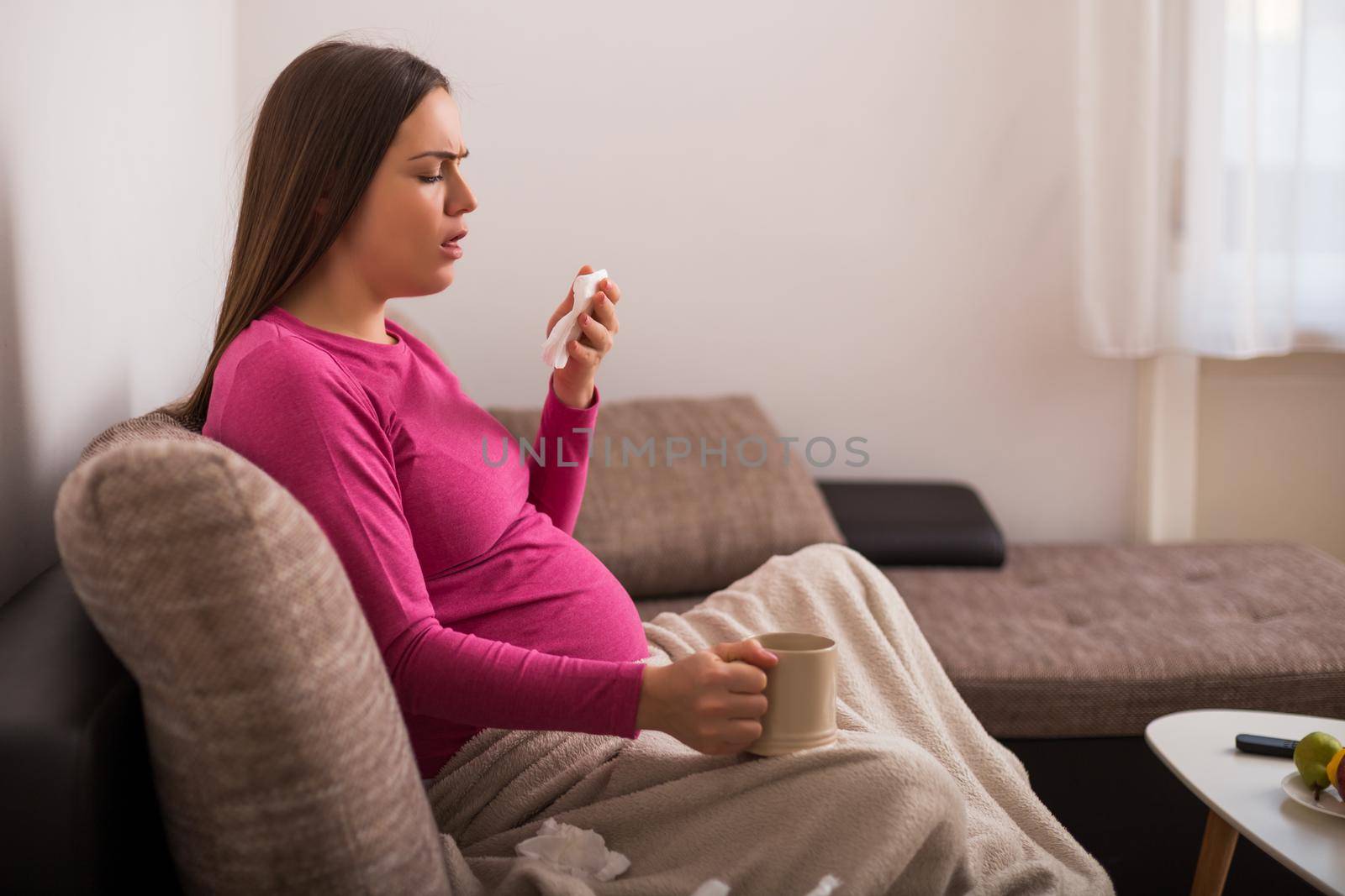 Exhausted pregnant woman coughing while having flu and drinking tea.