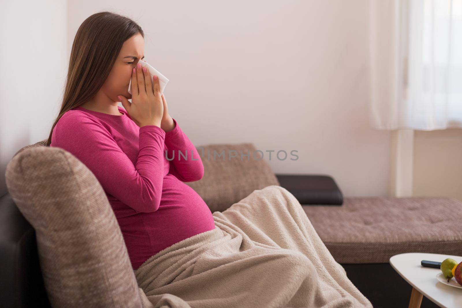 Exhausted pregnant woman having flu and blowing nose.