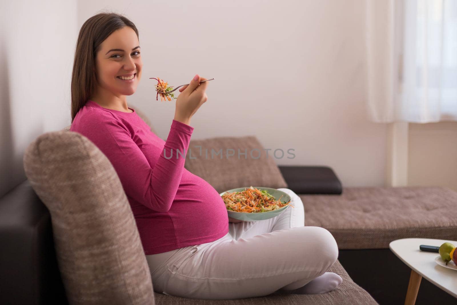 Happy pregnant woman eating salad.