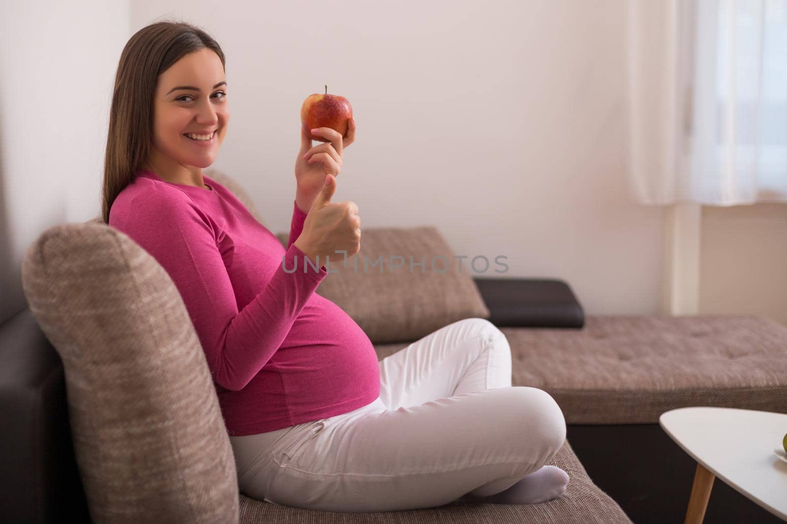Happy pregnant woman eating apple and showing thumb up.