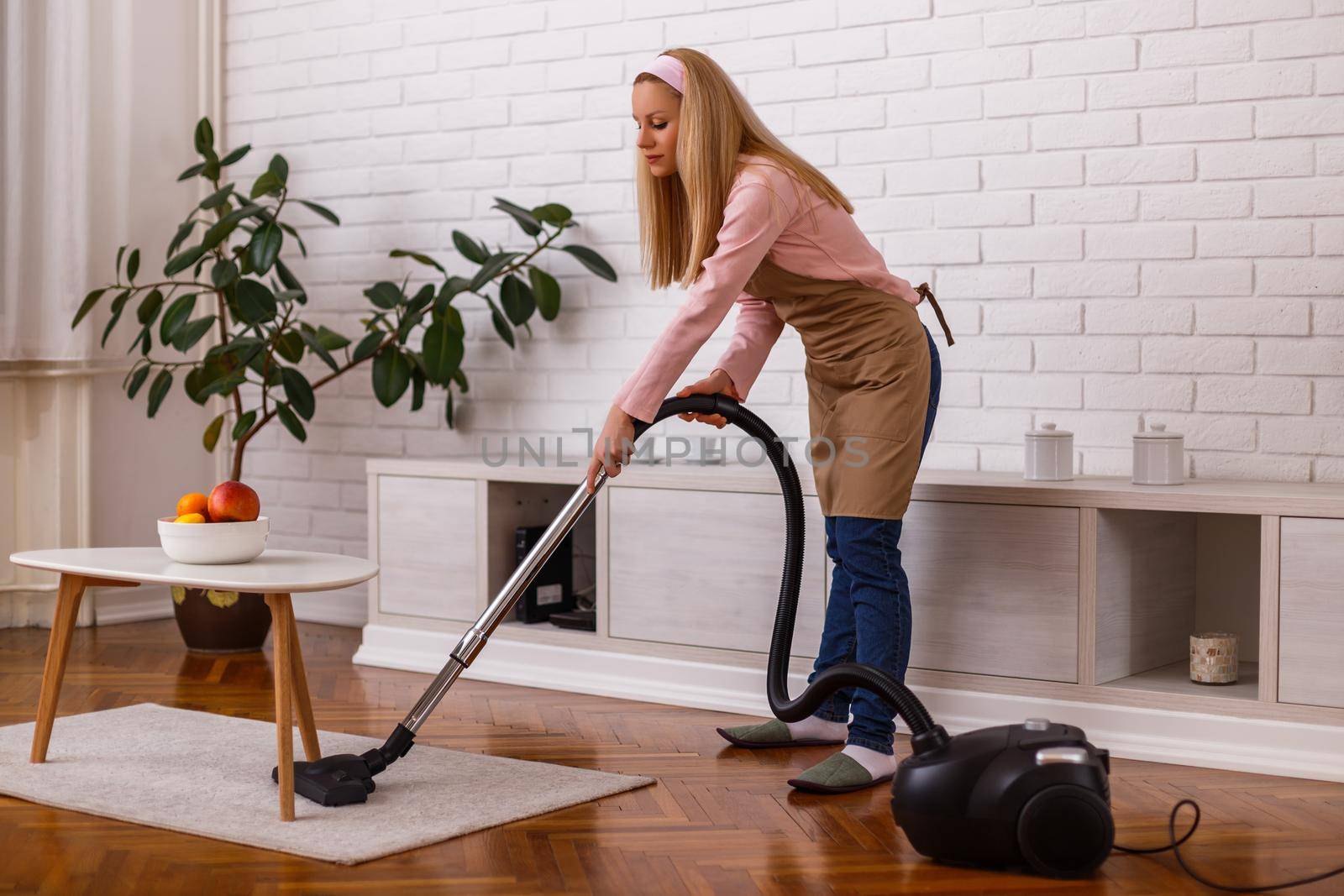 Beautiful housewife cleaning with vacuum cleaner her home.