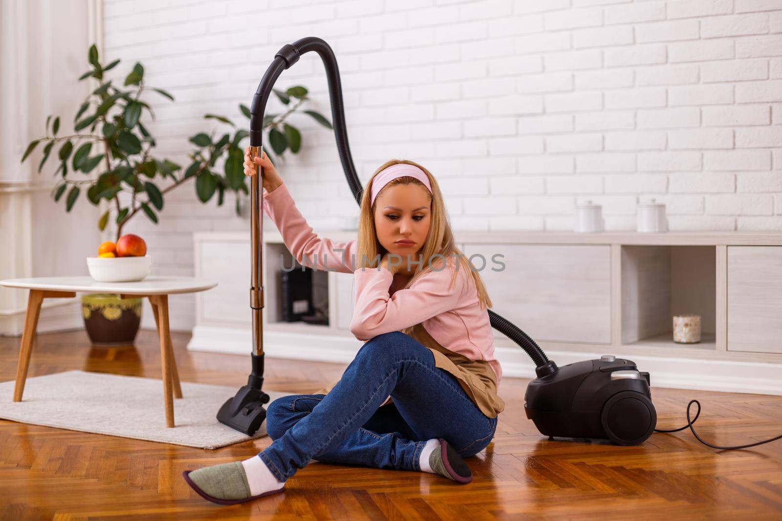 Image of angry and tired housewife with vacuum cleaner  in the living room.