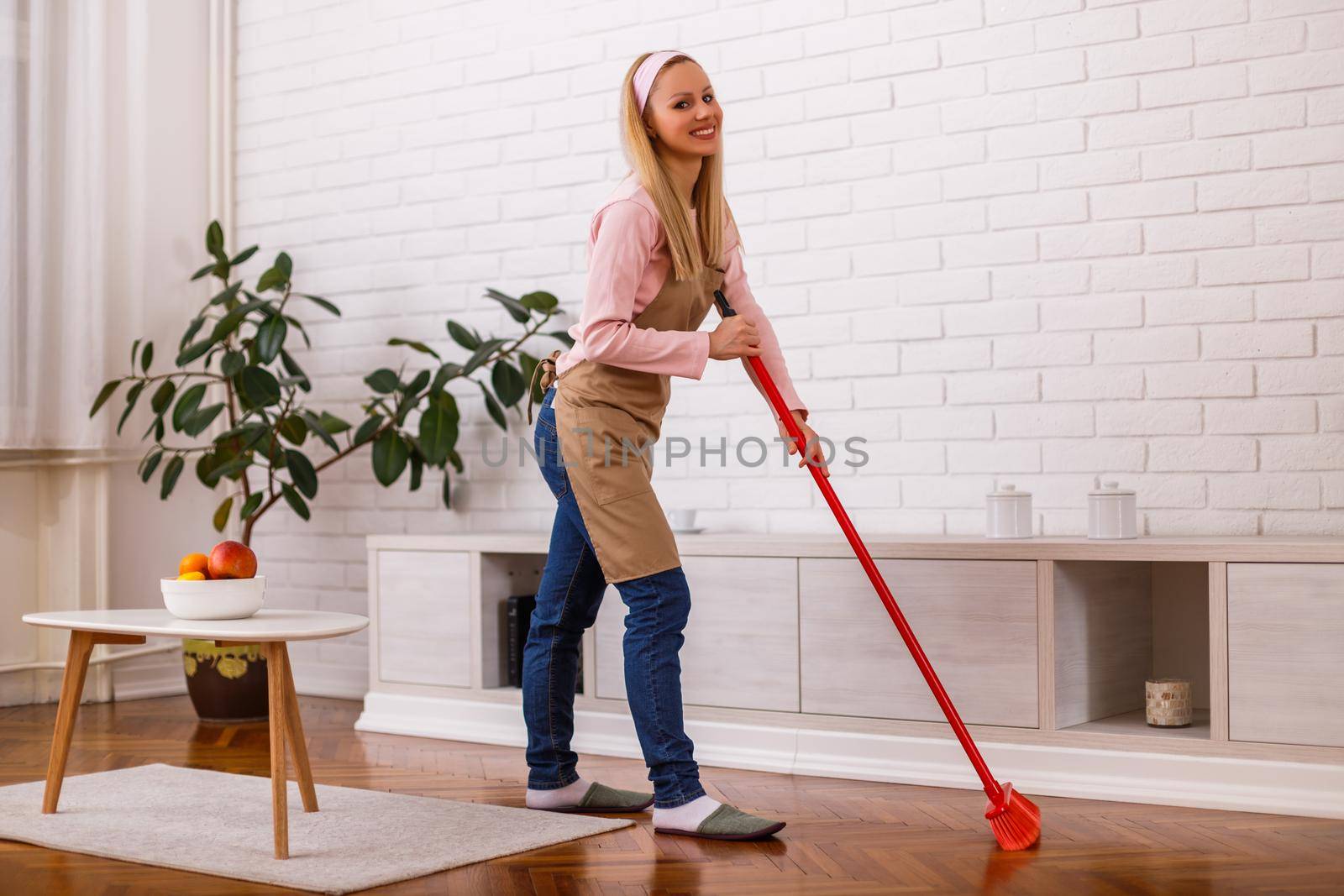 Beautiful housewife cleaning with broom her home.