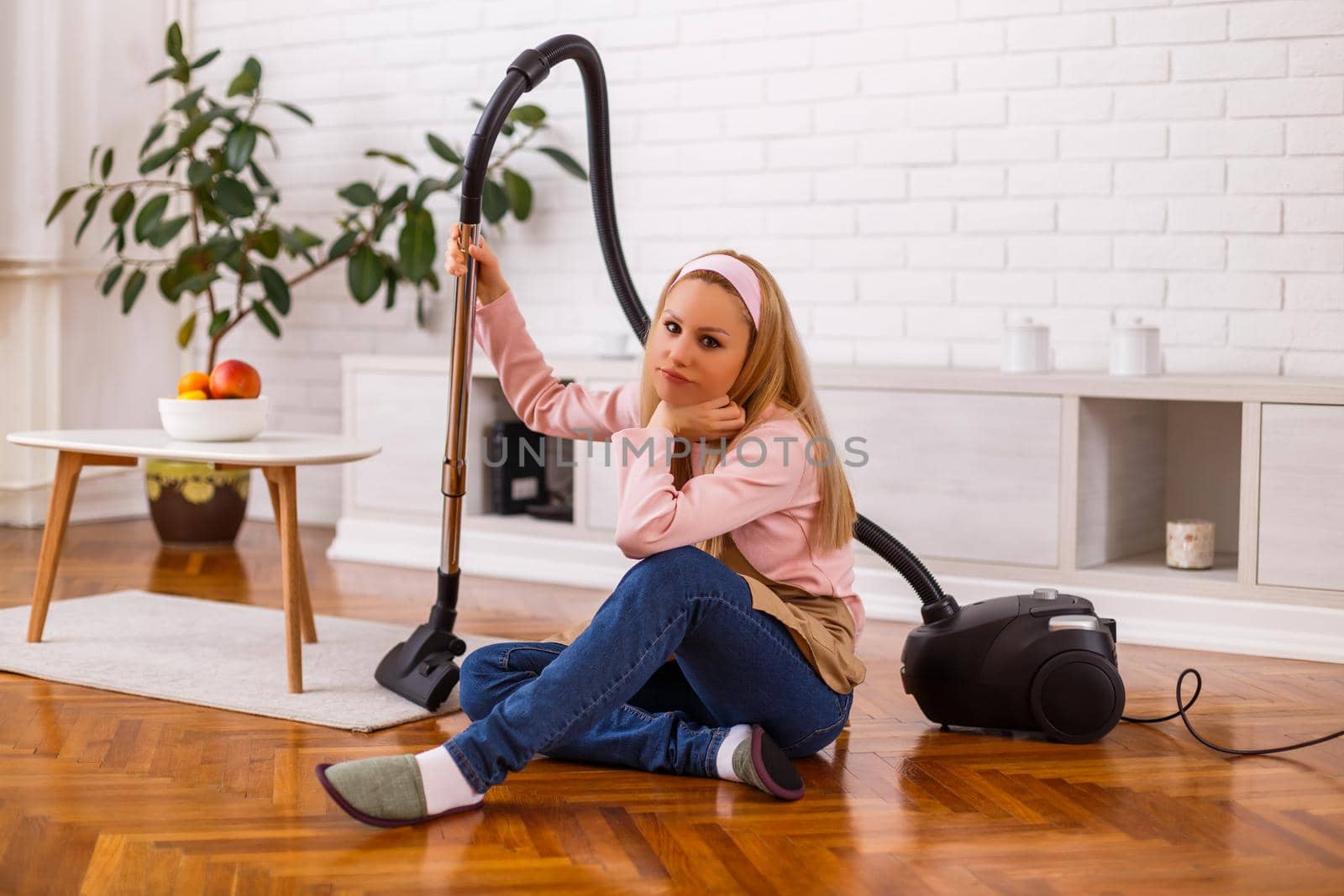 Image of angry and tired housewife with vacuum cleaner  in the living room.