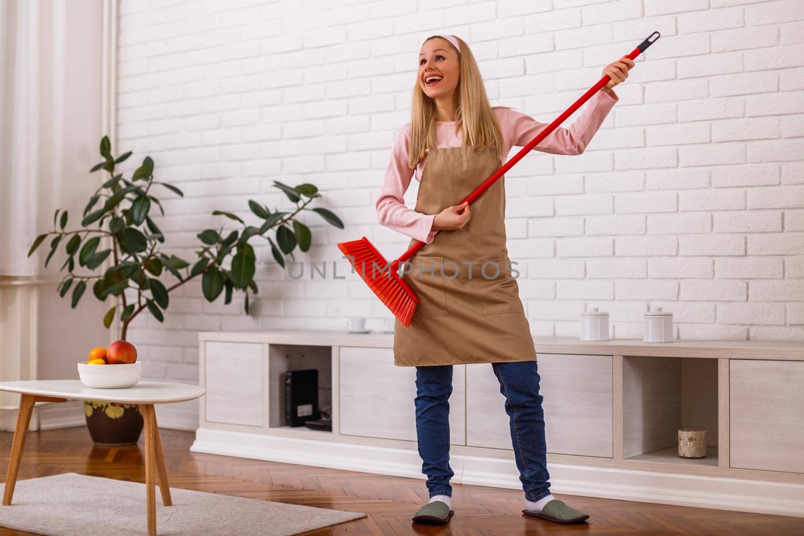 Beautiful cheerful housewife playing on her guitar broom while cleaning her home.