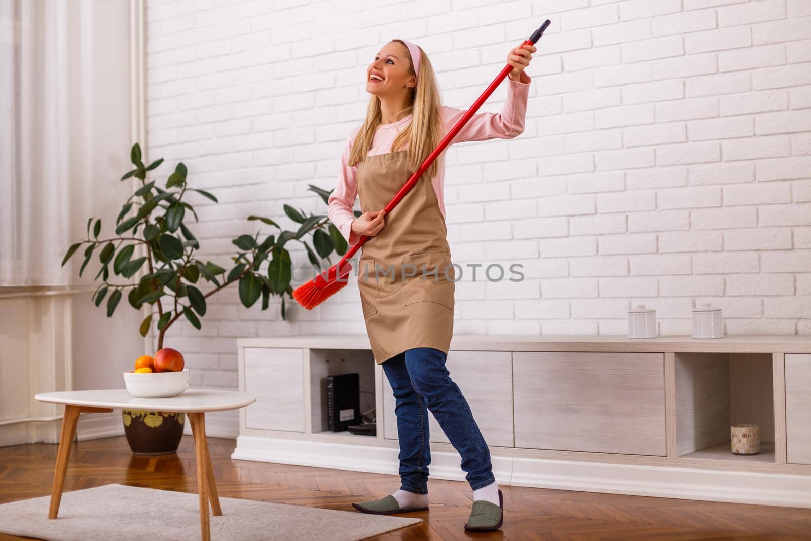 Beautiful cheerful housewife playing on her guitar broom while cleaning her home.