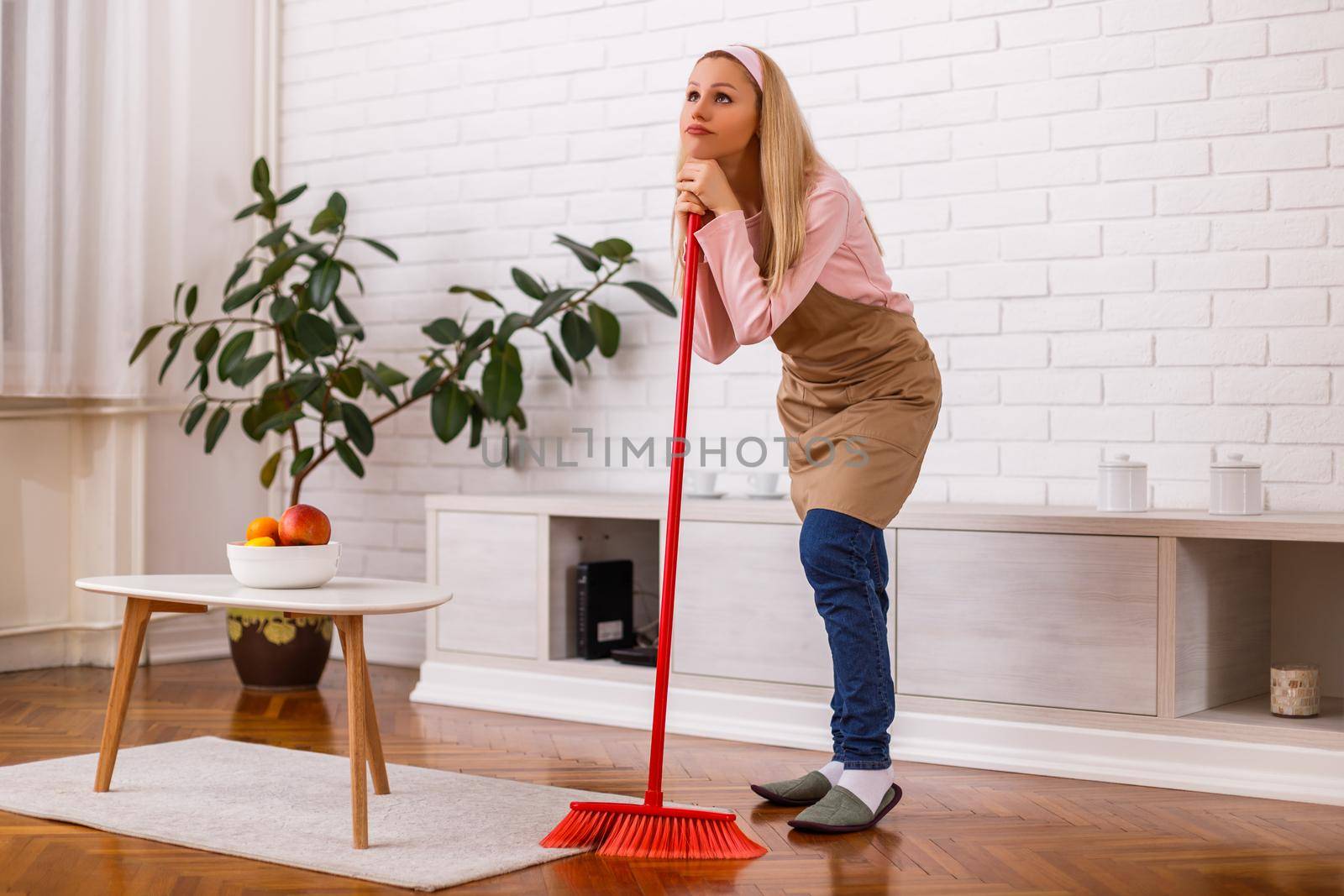 Tired housewife cleaning living room with a broom.