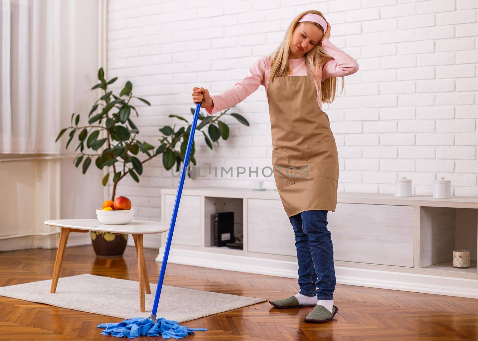 Tired housewife cleaning living room with a mop.