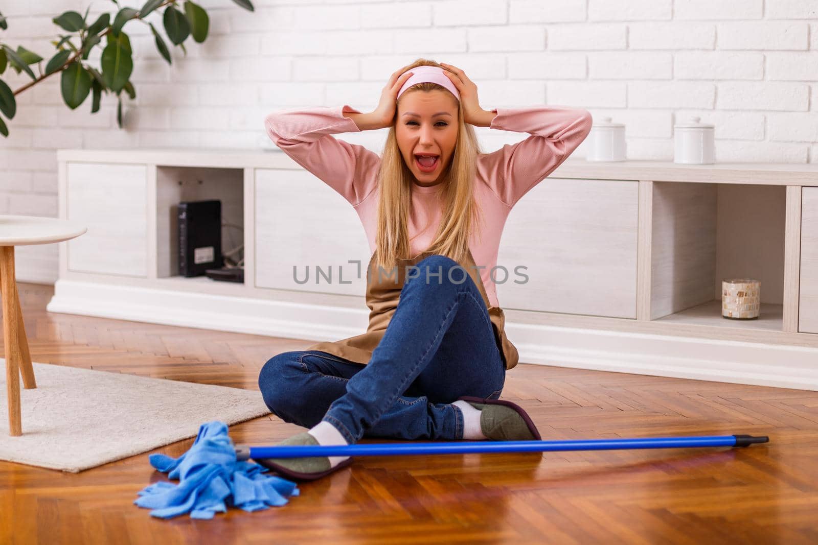 Image of  overworked housewife with mop shouting while sitting in the living room.