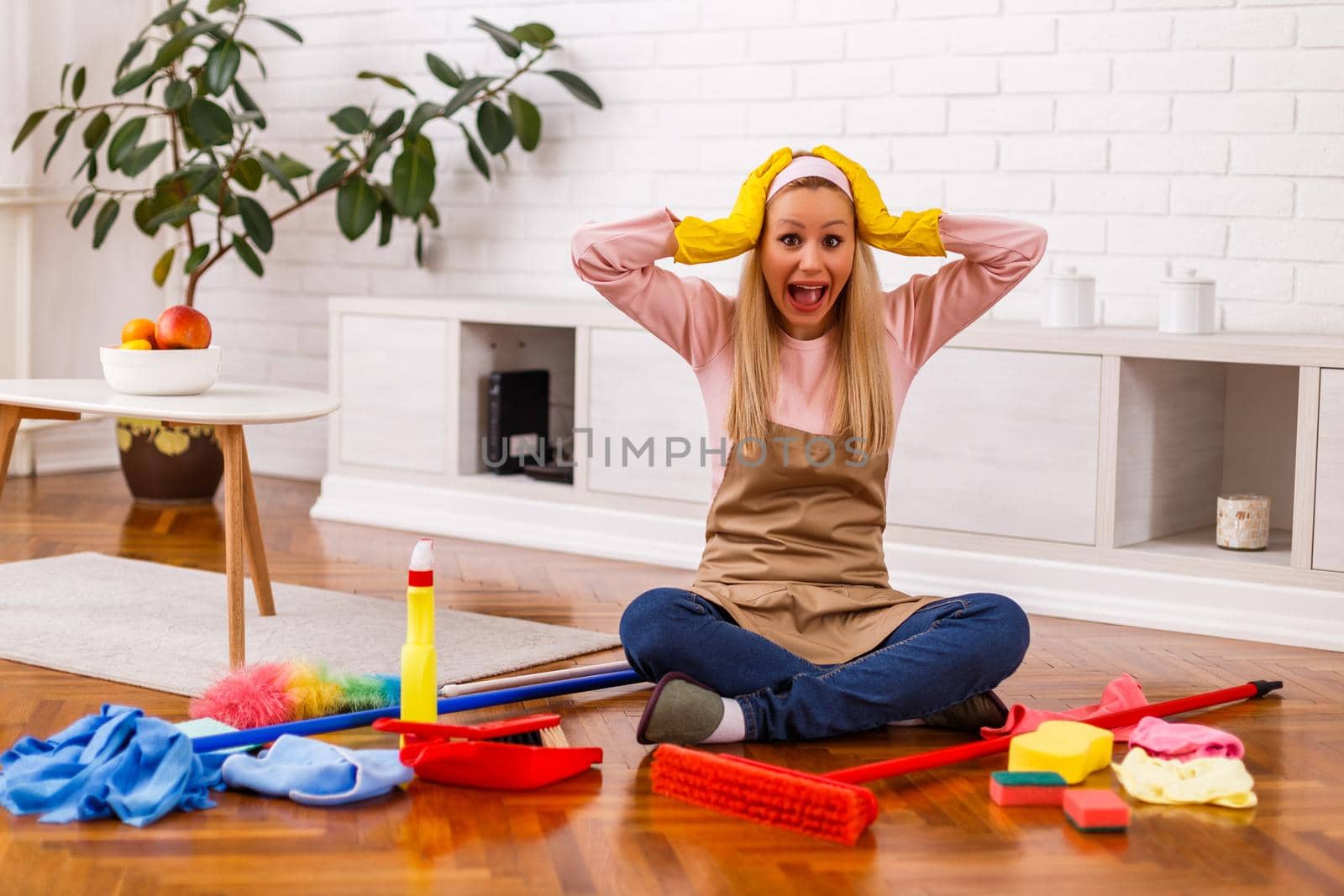 Image of  overworked housewife with cleaning equipment shouting while sitting in the living room.