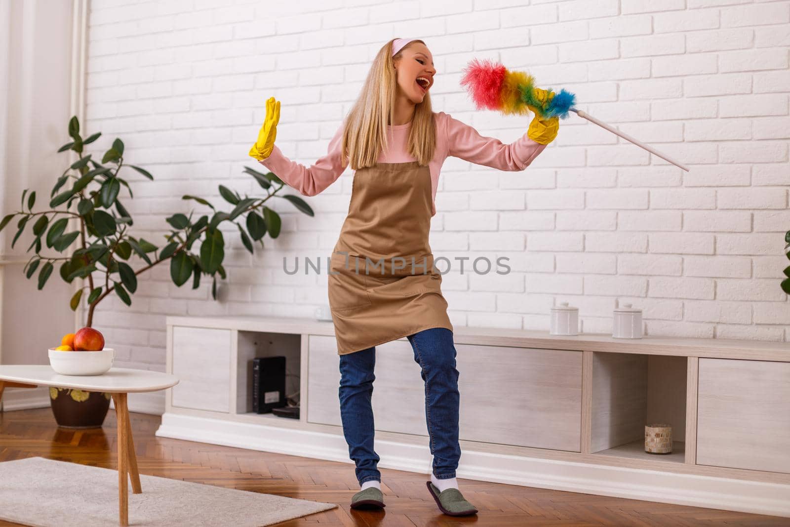 Beautiful housewife is singing while cleaning with duster her home.