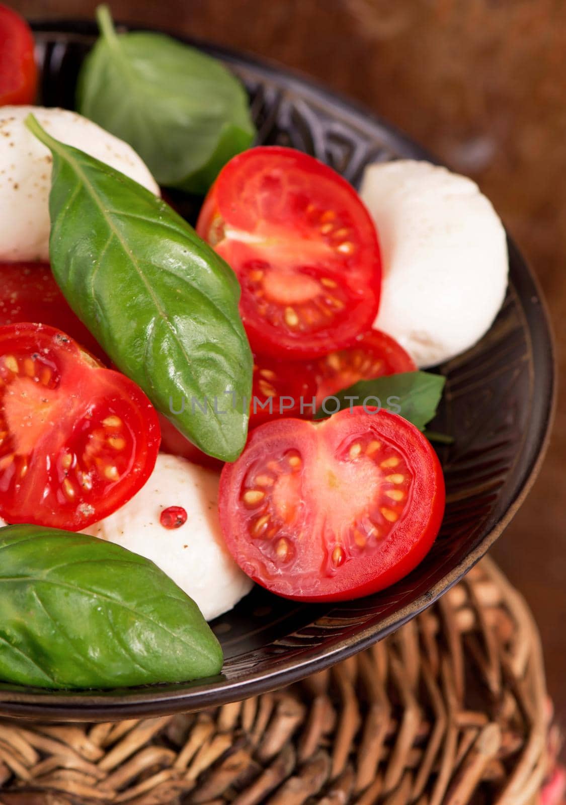 Round camembert cheese with cherry tomatoes and basil in a dark plate by aprilphoto