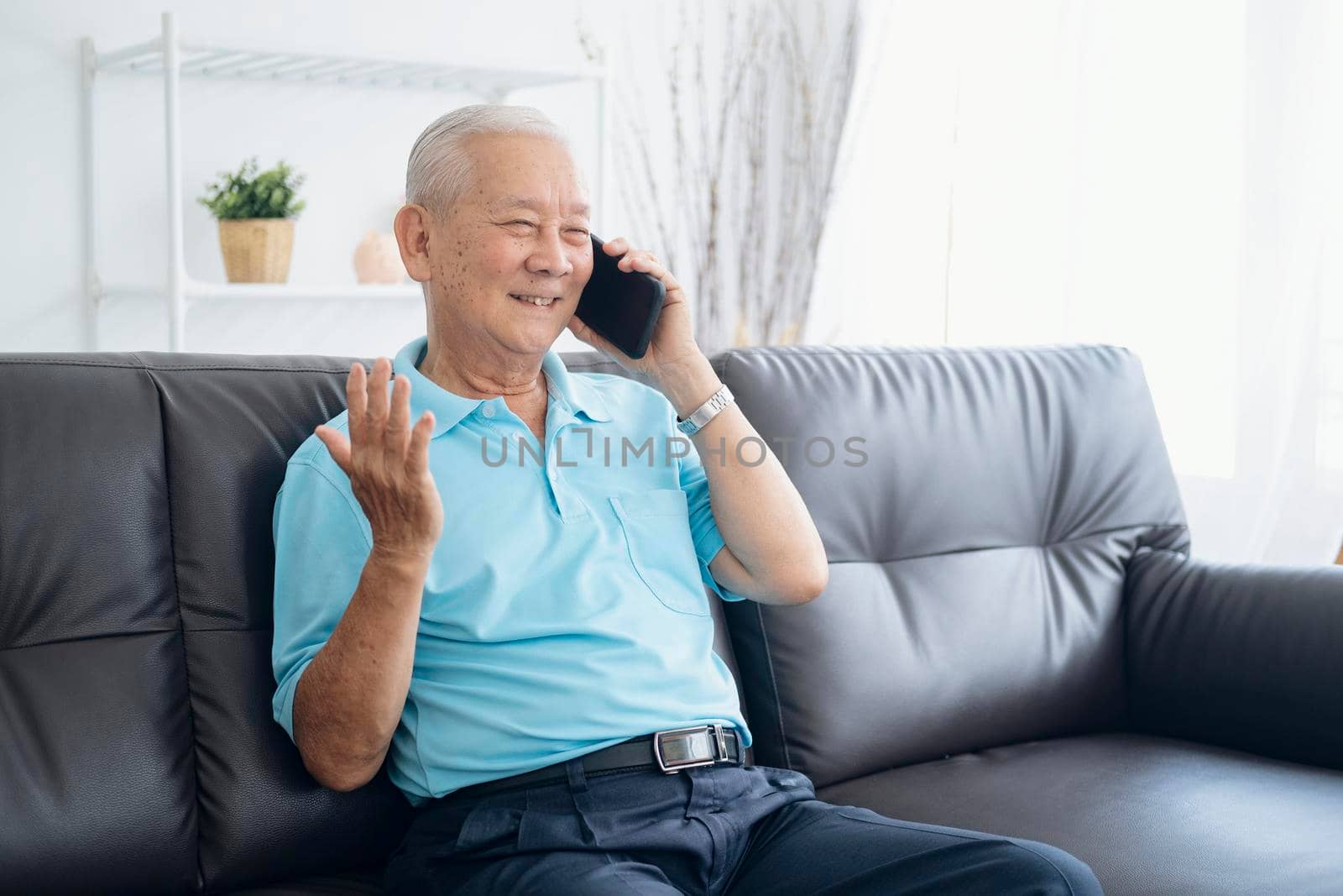 Cheerful senior man smiling while answering smartphone on couch at home porch. by ijeab