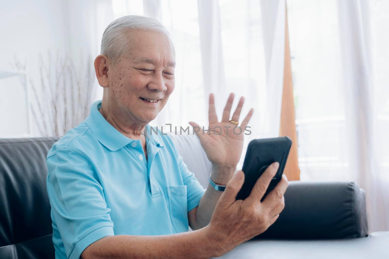 Elderly man making video call and waving at screen. by ijeab