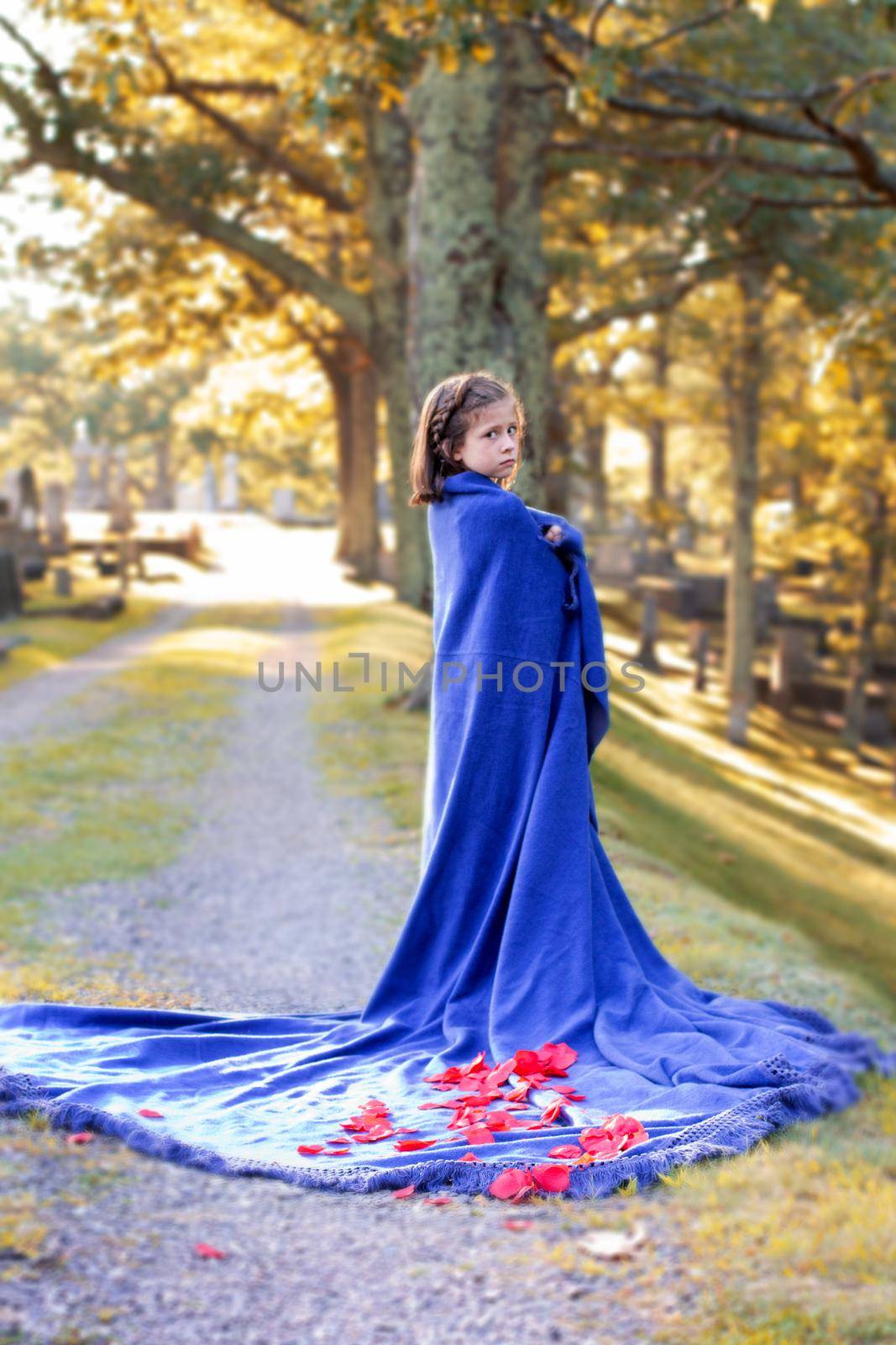 a young girl wrapped in a blanket with roses looks mournful in the cemetery 
