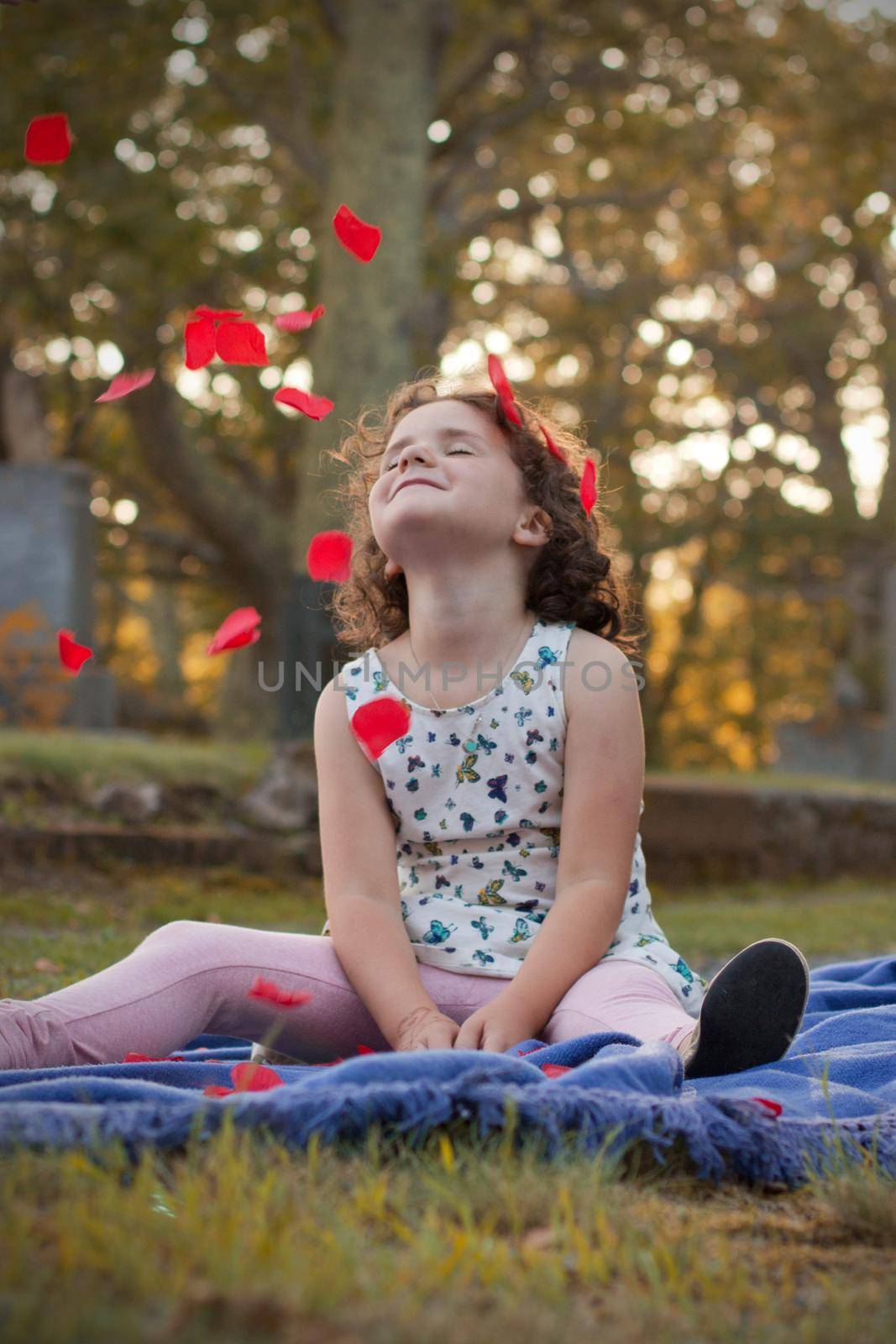 little girl with her face to the sun as rose petals fall on her face