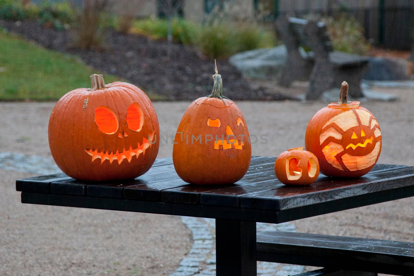 Four jack-o-lanterns or carved pumpkins with scary faces sit lit on a table. 