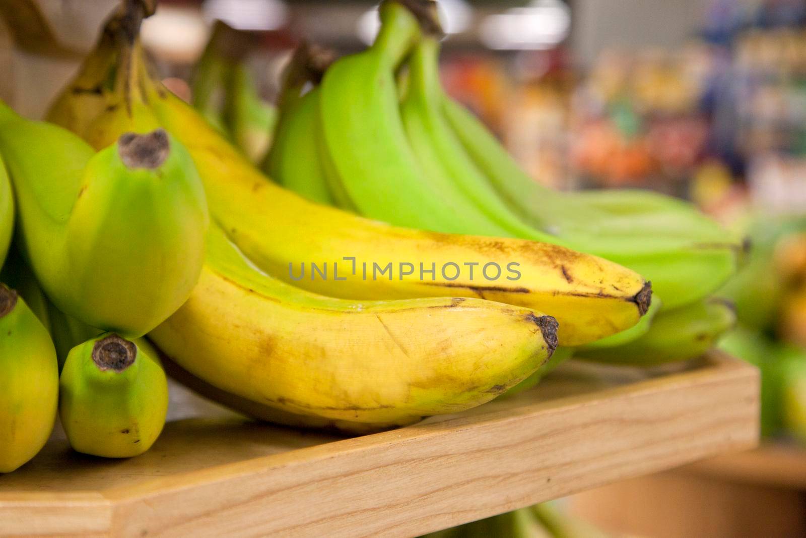  bunches of imperfect yellow and green bananas, in a store on a shelf 
