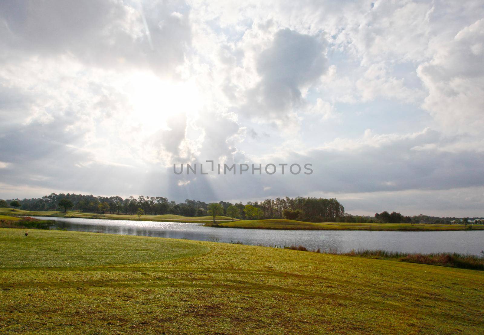 sun peeking through the clouds at early morning on a florida golf course beside a pond 