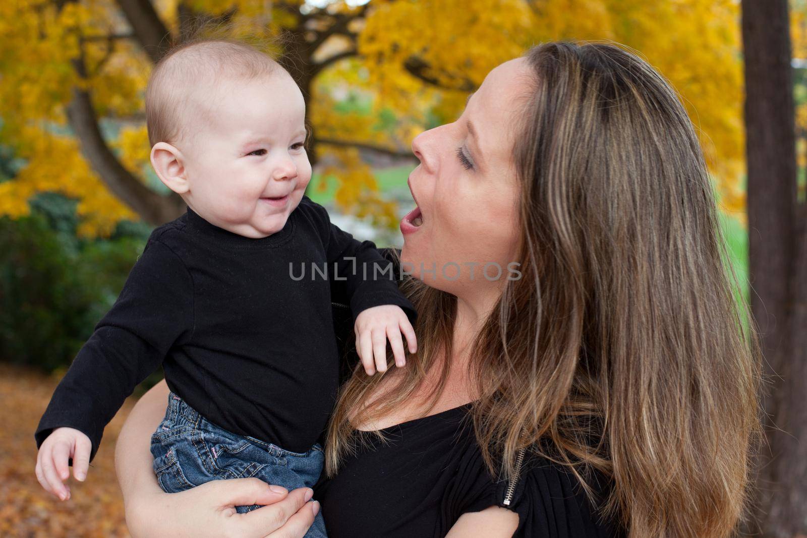 Portrait out of doors of mother and smiling baby, mother holding baby and talking  to her. 