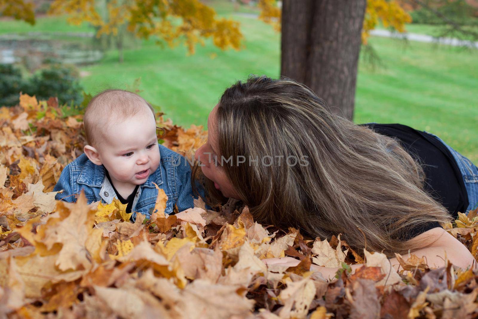 Portrait of mother and baby daughter playing among fallen leaves in the park in Autumn