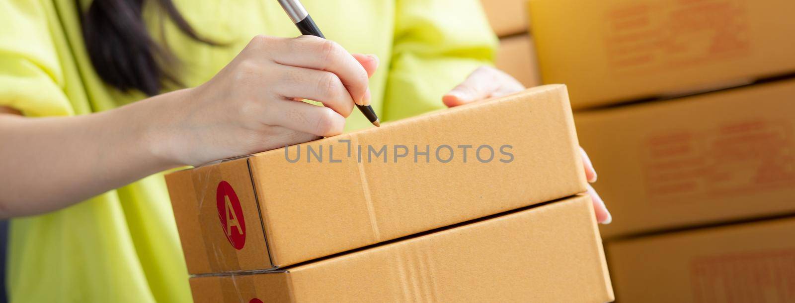 Closeup hand of young asian woman writing address on parcel box at home for delivery order to customer, shipping and logistic, merchant online and seller, business owner or SME, online shopping. by nnudoo