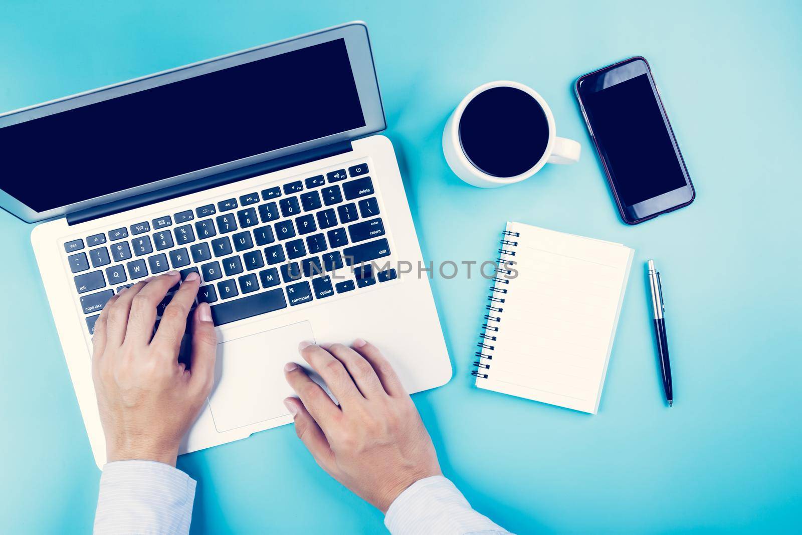 Hand of businessman working on laptop computer with phone and notebook on desk in office, hand typing keyboard with book and pen and smartphone, top view, flat lay, business and communication concept.