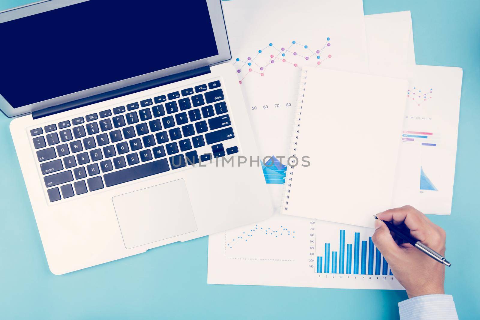 Hand of businessman looking documents report statistic financial with graph and chart and laptop computer and book on desk, finance and invest, digital marketing, business and communication concept.