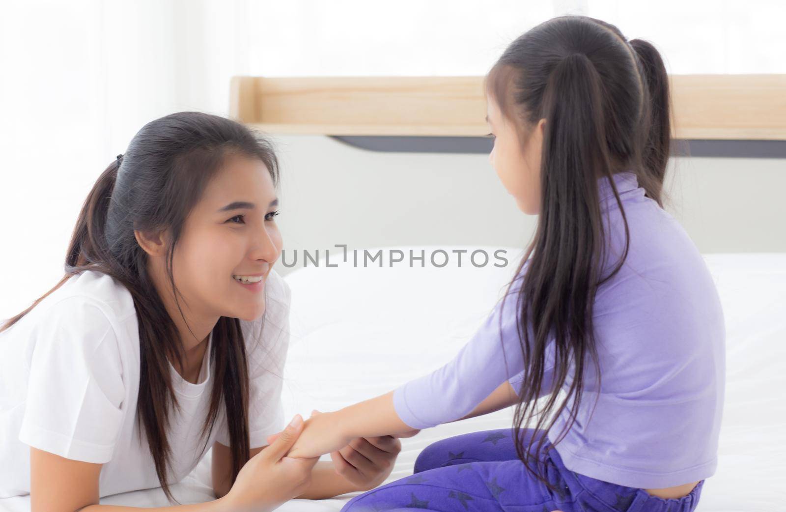 Young asian mom and daughter smiling and eye contact together with care in room, face of mother and girl looking eye with relationship and bonding, emotion and expression, family and love concept.