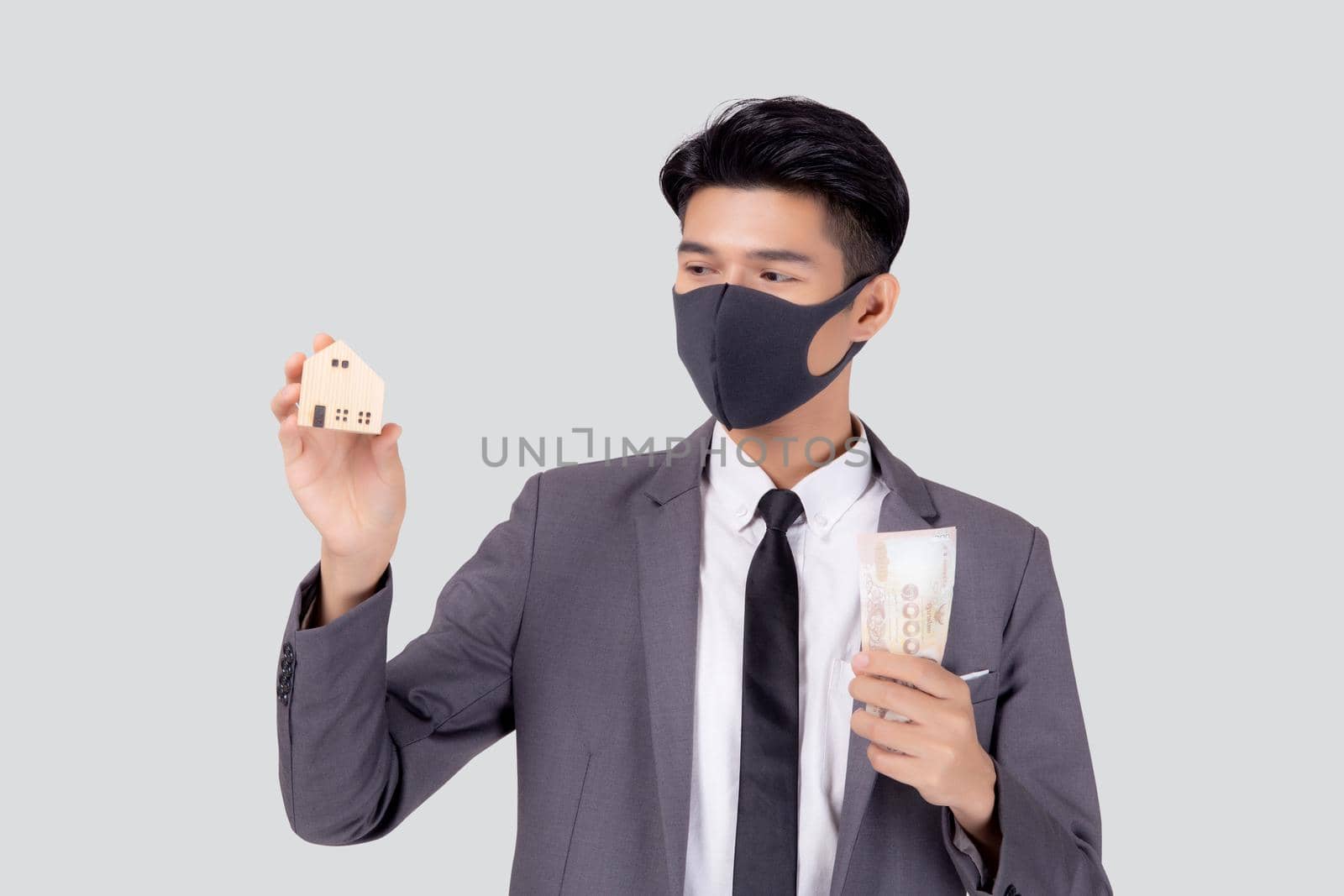 Young asian businessman in face mask holding money Thai and home isolated on white background, pandemic and crisis of economic, business man and investment property during disease covid-19.