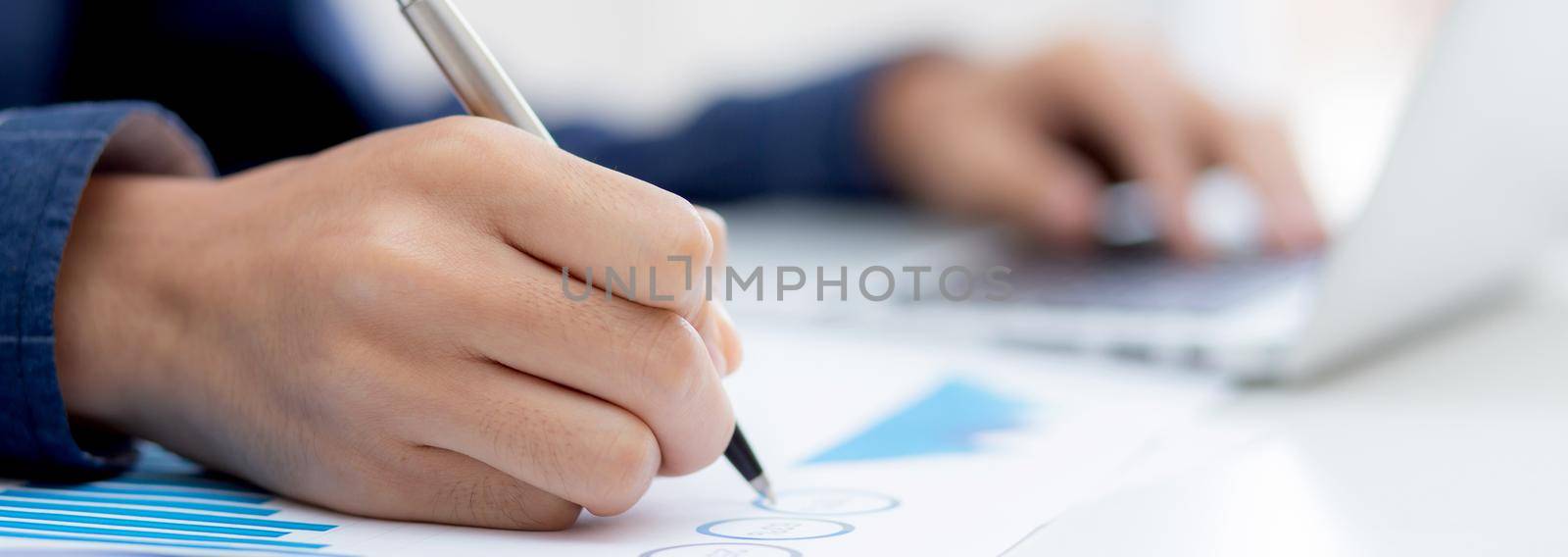 Closeup hand of business man writing on note while using laptop computer on desk at home, male planning on note for business success, author and blog, businessman working on table, employee and job. by nnudoo