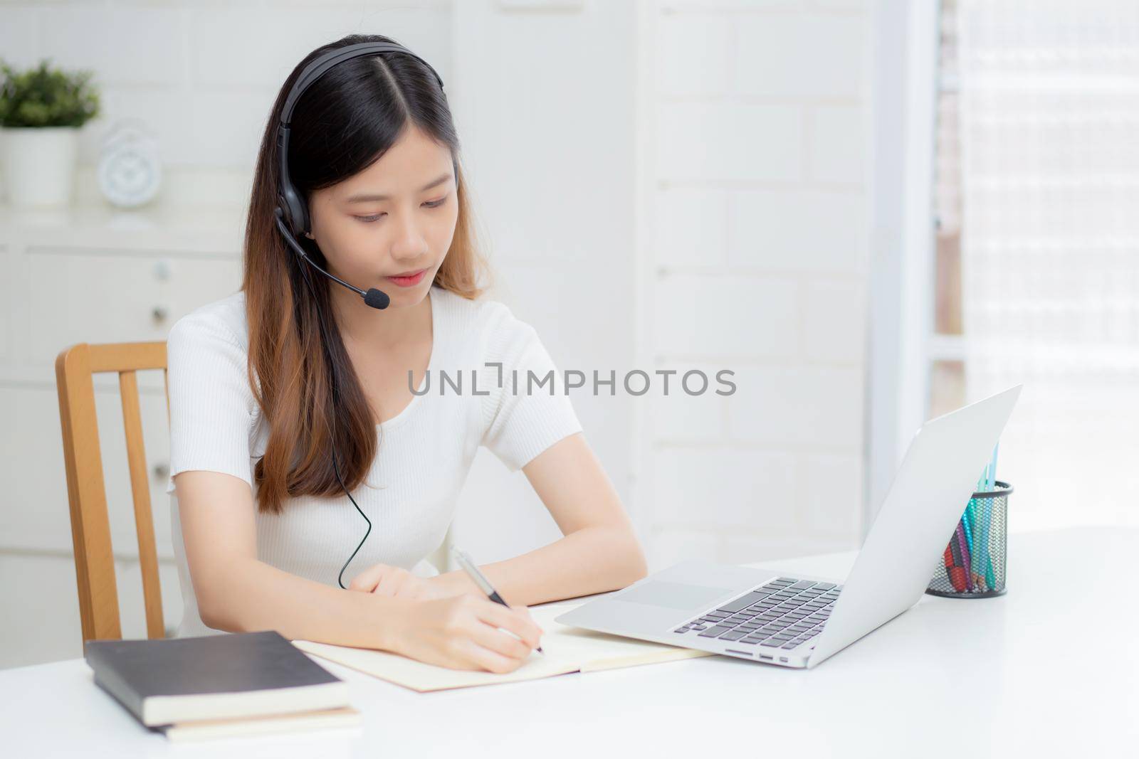 Young asian woman wearing headphone study online with e-learning on desk, girl wearing headset learning to internet with laptop computer at home, new normal, distance education and training.