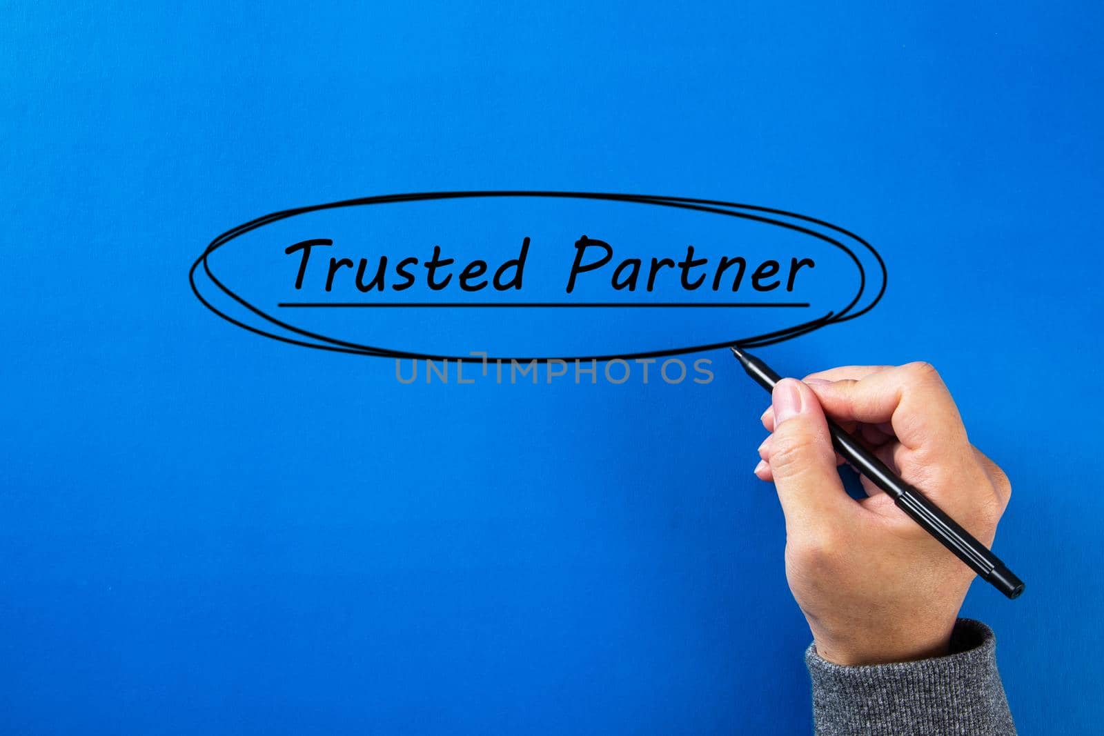 Businessman hand writing a Trusted partner sign with black marker over blue background.