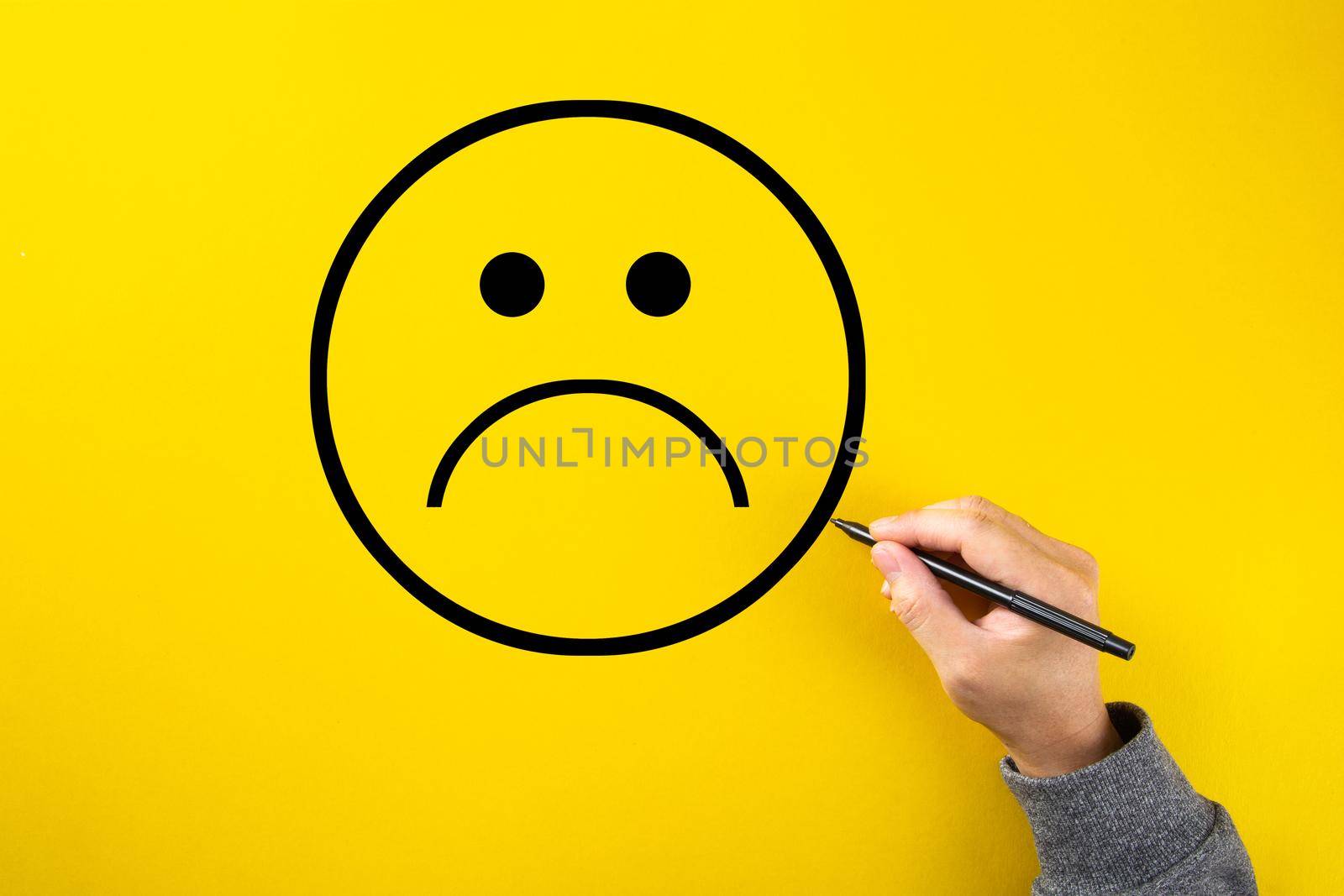 Male hand drawing a sad face sketch on yellow background. Client satisfaction, service or product evaluation concept.