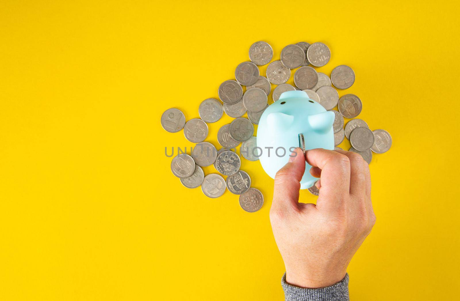 Hand puts a coin into the piggy bank coin on a yellow background.