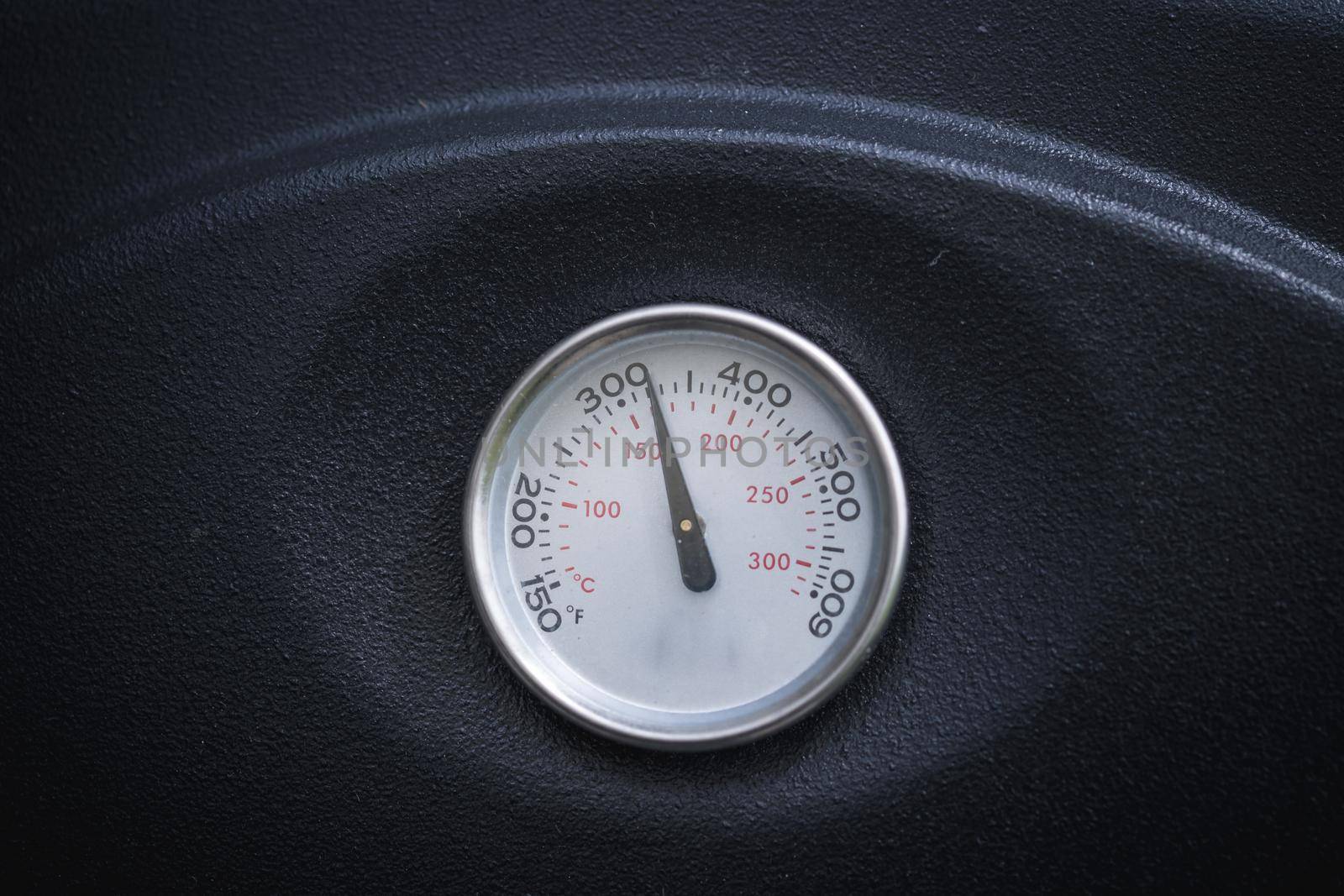 Close up of barbecue or smoke grill circular thermometer, black surface