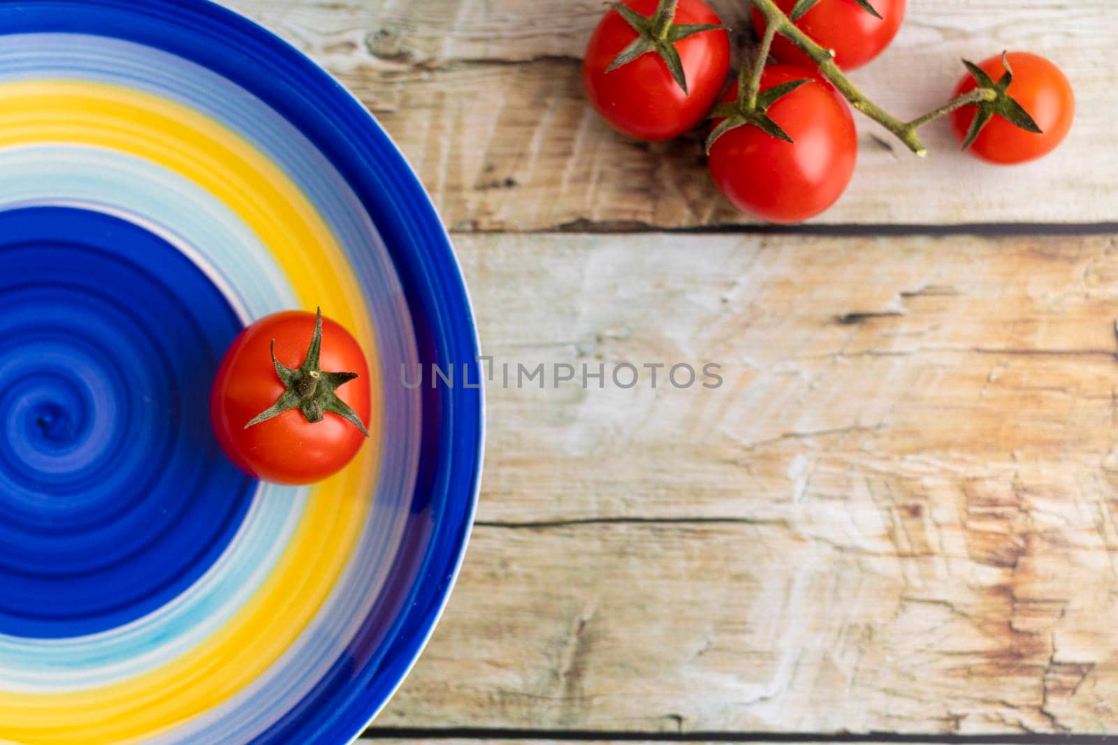 Cherry tomatoes on colorful striped plate and brown wooden background