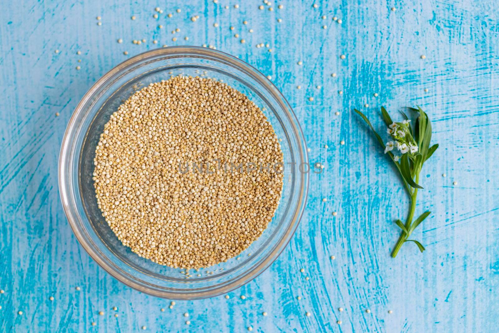 Raw quinoa grains inside transparent bowl, on blue table