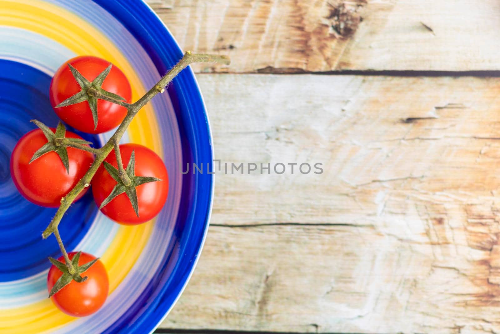 Cherry tomatoes on colorful striped plate and brown wooden background