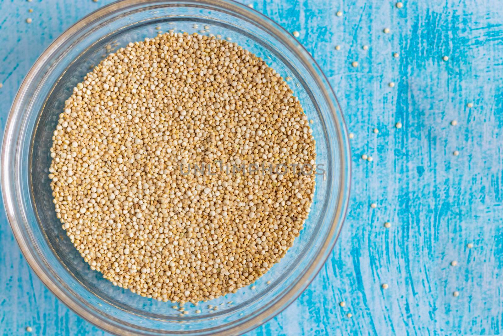 Raw quinoa grains inside transparent bowl, on blue table by eagg13