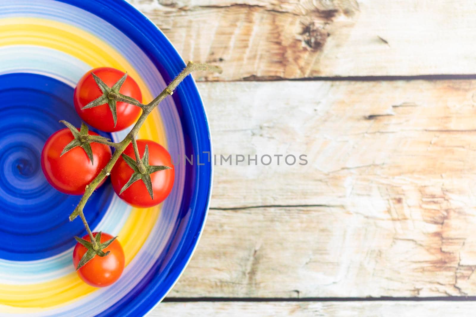 Cherry tomatoes on colorful striped plate and brown wooden background