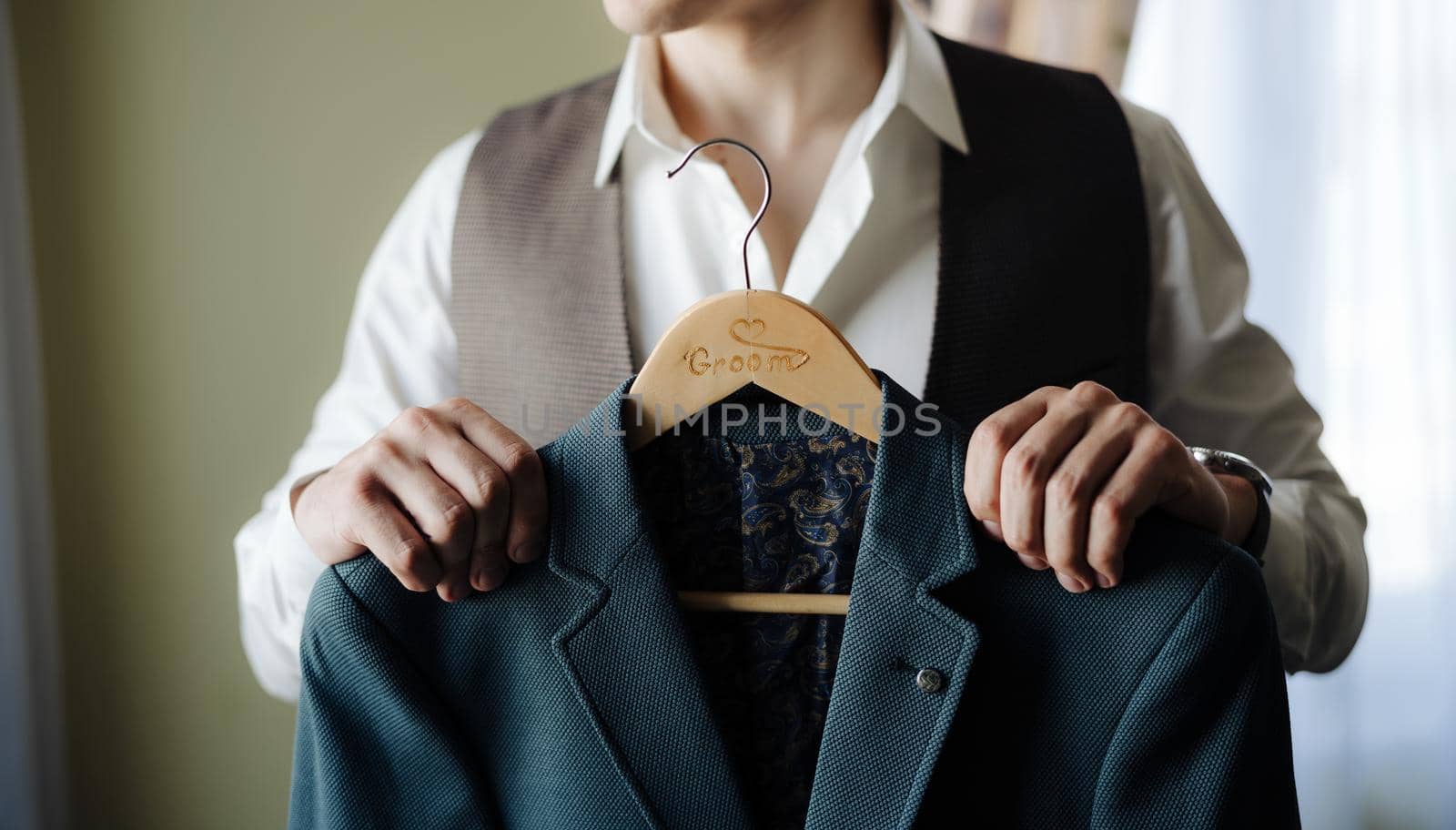 Groom in a white shirt and vest holds a jacket on a hanger. High quality photo